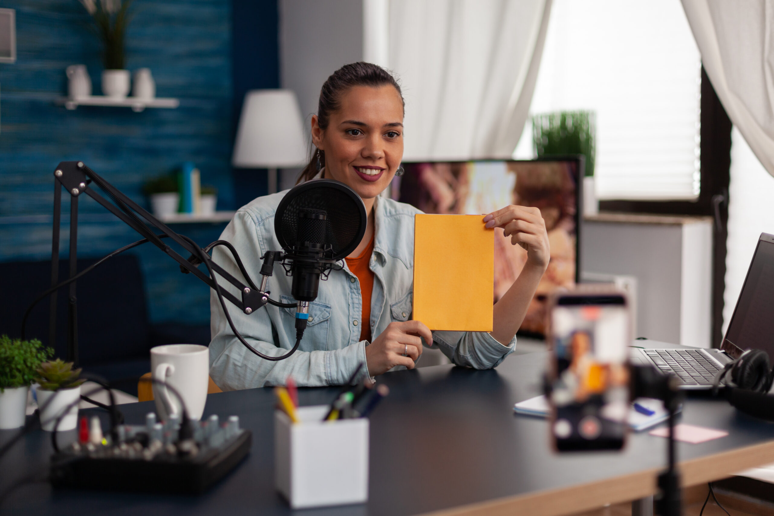 Woman influencer presenting yellow product box in front of recording smartphone.